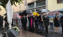 Il piazzale dove fu ucciso un anno fa, da oggi intitolato a don Roberto Malgesini. Il sindaco, sotto la pioggia: "Anche il cielo piange"