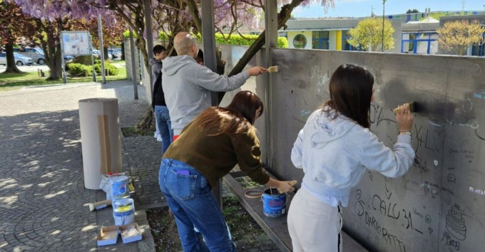 Giovani al lavoro per ripulire il muro della scuola dopo i vandalismi